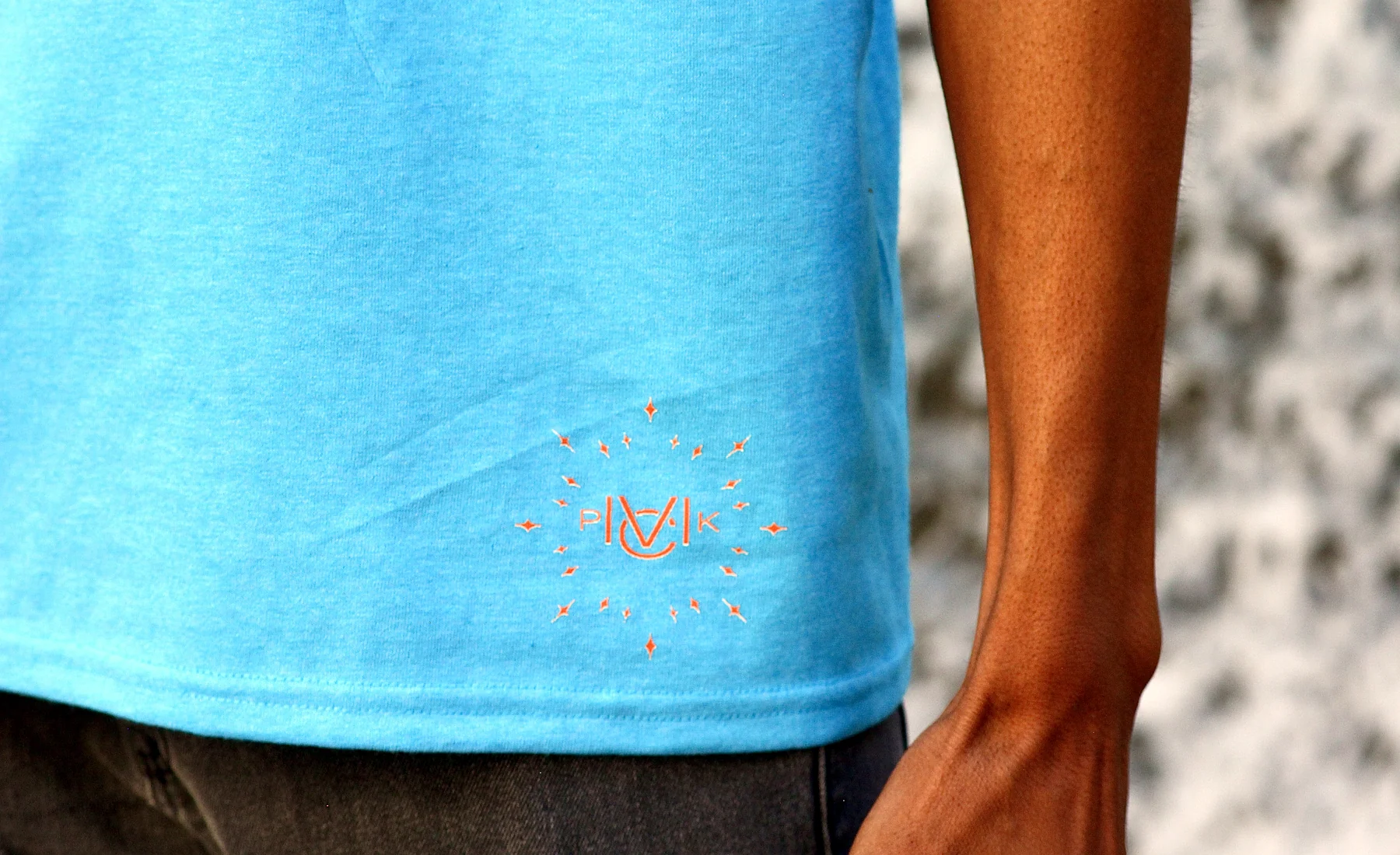 Close up of the orange MVCK PVCK monogram embroidered on the hem of the City of No Limits tee